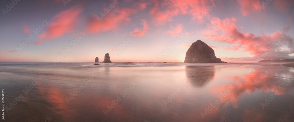 Wall mural The Sunset at Cannon Beach with Dramatic clouds in the background and a nice reflection in water. 
Dramatic coastal seascape featuring scenic rock formations Haystack Rock Oregon, USA