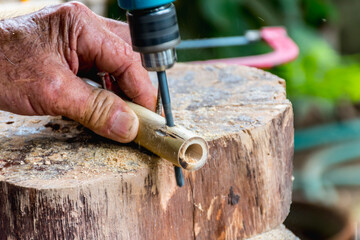 A carpenter uses a drill to drill holes in bamboo to make crafts.