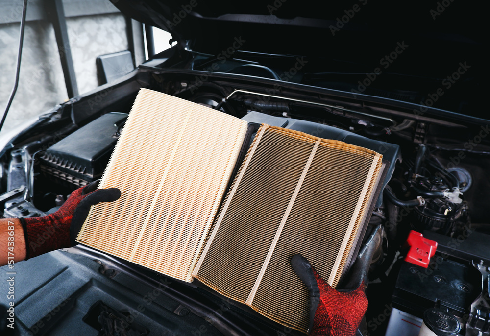 Wall mural auto mechanic compares a clean new air filter to an old, filthy one with a engine compartment backgr