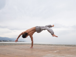 Fototapeta premium Shirtless caucasian man doing backflip on pebble beach. 