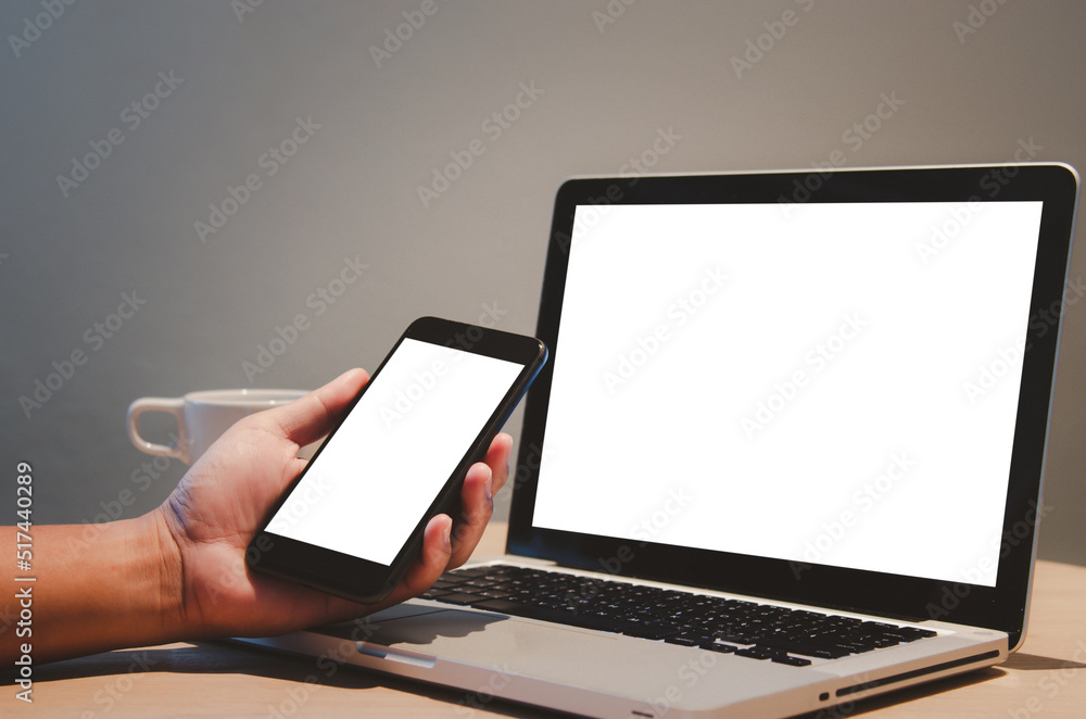 Poster man hand holding mobile smartphone and computer laptop mock up blank screen on desk.