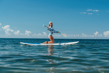 Woman sup sea. Happy healthy fit woman in bikini relaxing on a sup surfboard, floating on the clear...