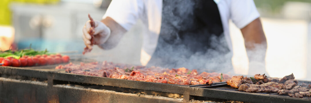 Professional male chef frying fresh meat on grill on open air