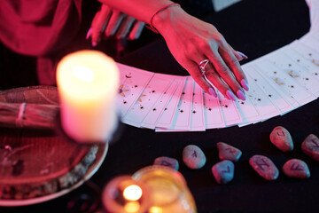 Closeup image of fortune teller predicting fate with tarot cards in darl room with burning candles