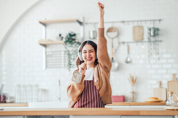 Happy carefree asian woman wearing headphones and ladle singing have fun moving listening to music...