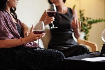 Young woman with red thread on wrist that helps to ward off misfortune drinking wine and talking to best friend