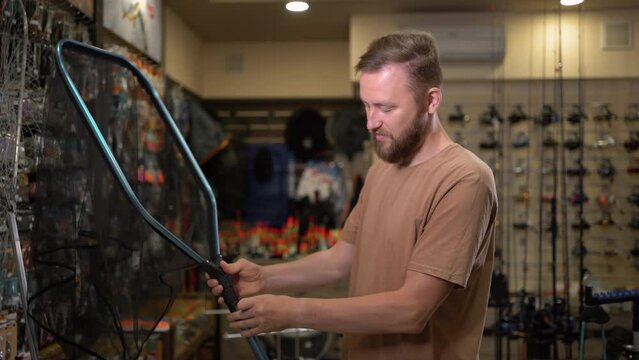 young bearded caucasian male fisherman in a fish tackle shop chooses a landing net for fishing. stacks and checks the fisherman's inventory.