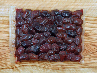 greek kalmata olives in vacuum packaging on olive wood board, traditional souvenir to eat at home
