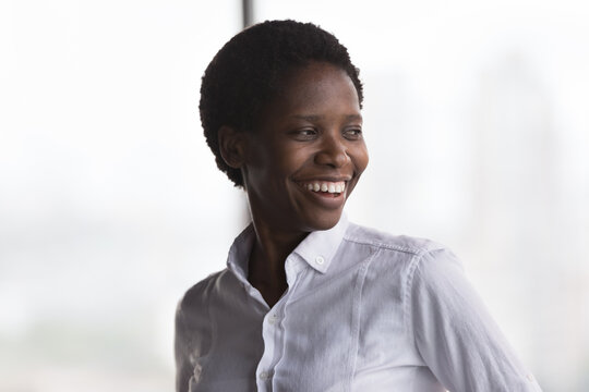 Happy cheerful African American business leader woman looking away with toothy smile, thoughtful face, dreaming, thinking of career, project success, future vision