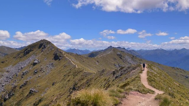 Static off center, hiker approaches on exposed alpine trail, vast mountain landscape, Fiordland, Kepler Track New Zealand