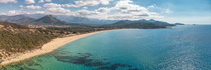 Panoramic aerial view of the sandy beach at Losari and turquoise Mediterranean sea on the west coast of Corsica with mountains and Ile Rousse in the distance © Jon Ingall