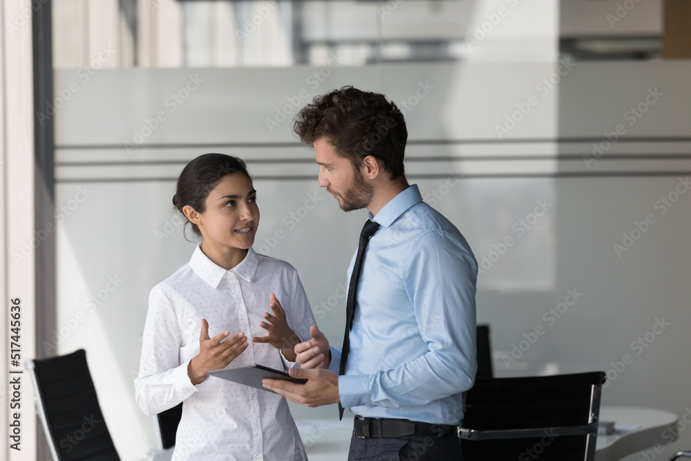 Sticker two engaged diverse managers in formal clothed discussing business project, talking in office, using