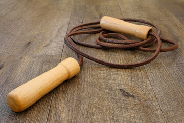 Leather skipping rope with wooden handles coiled on wooden floorboards