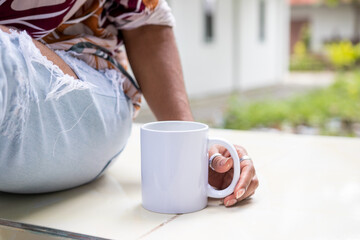 mockup of a white blank mug featuring a woman placed it beside her