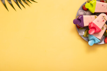 Homemade ice cream from molds on plate with ice and pieces of fruit on colored background and palm leaves with copy space. Top view. Summer food background