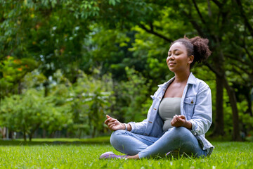 African American woman relaxingly practicing meditation in the forest to attain happiness from...