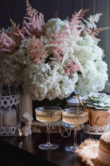 A bouquet of white hydrangeas and pink astilba, succulent, candles and a fashionable glass for dessert and champagne with wine inside. Cozy interior. The concept of a party, wedding and holiday.