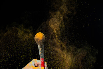 Woman shaking off orange powder from a brush on a black background. 