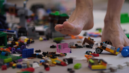 barefoot man walks among the scattered toys. Foot stepping on children's toys. Scattered toys on the floor. concept of an abundance of toys in the modern world.
