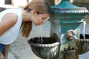 Heat waves concept. Portrait of young woman hydrates herself drinking water from a fountain during a summer hot day. - obrazy, fototapety, plakaty
