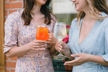 Close up of happy women drinking cocktails outdoors on sunny day. Limoncello tonic and aperol...