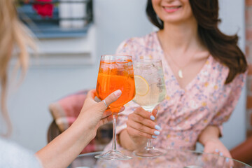 Close up of happy women toasting glasses of cocktails on the terrace of the cafe. Fresh summer drinks.