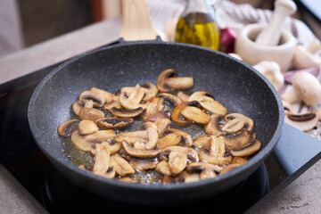 Sliced mushrooms in a frying pan on induction hob at domestic kitchen