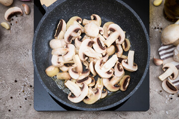 Sliced mushrooms in a frying pan on induction hob at domestic kitchen