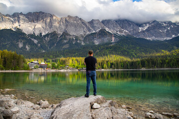Fototapeta na wymiar Young man sitting on a stone near the Eibsee Lake, Germany. Travel, lifestyle concept.