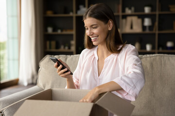 Happy woman unbox parcel box, check ordered items in phone use retail ecommerce application, leave positive feedback to customer, feel satisfied with delivered goods, quick delivery services concept - obrazy, fototapety, plakaty