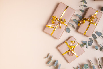 Gift boxes wrapped in kraft paper with golden ribbon and eucalyptus on pastel beige background. Holiday present concept. Top view