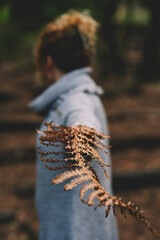 Back view of a woman holding and showing big arid leaf. Climate change and global warming future concept. People and environment. Earth planet care. Outdoors leisure activity at the park
