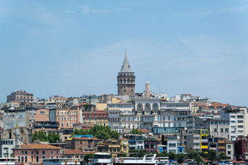Galata Tower behind buildings front side view from Golden Horn, travel concept in Istanbul city, beautiful landscape, known as Galata Kulesi, old historical structure in Istanbul, buildings and sky