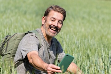 Happy smiling man in cereal field taking selfie with cell phone.