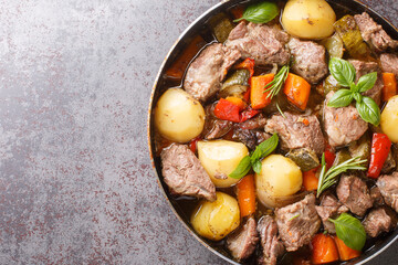 Traditional meat peka with potatoes, carrots, onions, peppers and zucchini and herbs close up on the table. horizontal top view from above