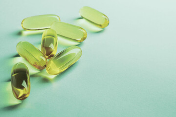 Yellow softgels lie on a green surface. Fish oil. Vitamins and a healthy lifestyle. Background or backdrop. Copy space. Softgel closeup. Omega-3 fatty acids capsule. Macro
