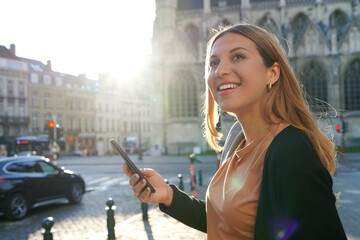 Portrait of young woman on side of road waiting a taxi cab holding a smart phone. Calling a taxi with a phone app concept.