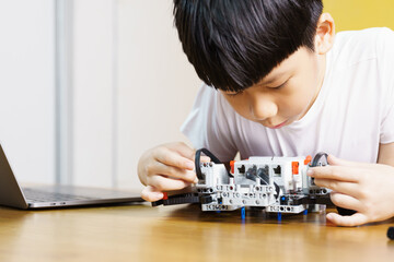 Smart looking Asian student kid assembling robot, coding and solving engineering problem at home...