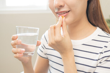 Dietary Supplement, Nutrition asian woman, young hand in holding yellow pill, talking daily vitamin D, E, A, fish oil pill for hair and skin with glass of water. Diet healthy eating, beauty people.