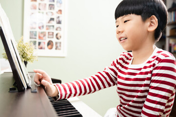 Cute Asian elementary child learning piano online class, using computer tablet, smiling and talking...