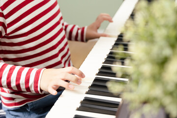 Close up of elementary school child's hand wearing red stripe long sleeve playing and practicing piano at home. Child brain development, music therapy and education.