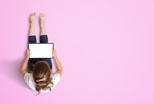 Child Sitting And Working On The Tablet. White Screen For App Or Game Promotion Mockup. Free Space For Copy On Pink Background. View From Above