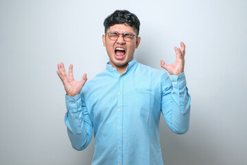 Naklejka premium Young asian man wearing casual shirt crazy and mad shouting and yelling with aggressive expression and arms raised. Frustration concept.
