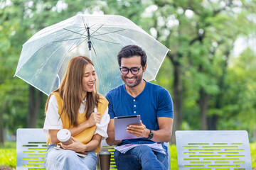 Young Asian and Indian couple enjoy having relaxing time in the rain together in the public park...