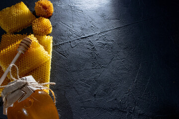 Honey in a jar and a honeycomb. On a black wooden background. Free space for text. Top view.