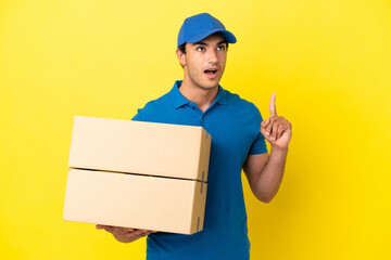 Delivery man over isolated yellow wall thinking an idea pointing the finger up