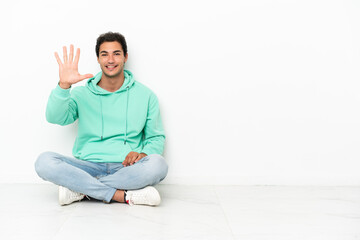 Caucasian handsome man sitting on the floor counting five with fingers