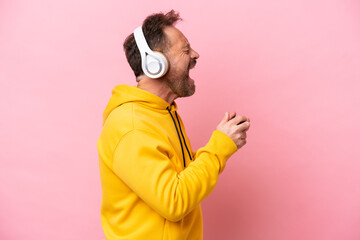 Middle age man playing with a video game controller isolated on pink background laughing in lateral position