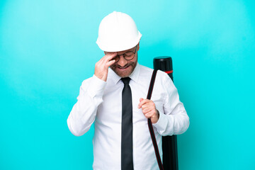 Middle age architect man with helmet and holding blueprints isolated on blue background laughing