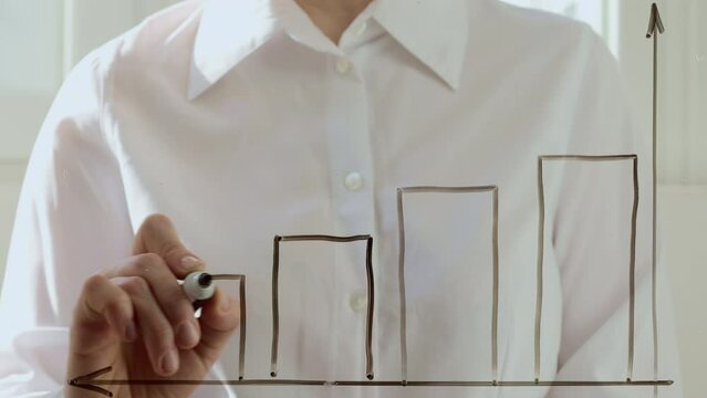 A business woman draws a financial chart and a falling down arrow on the glass. The concept of risk and crisis.